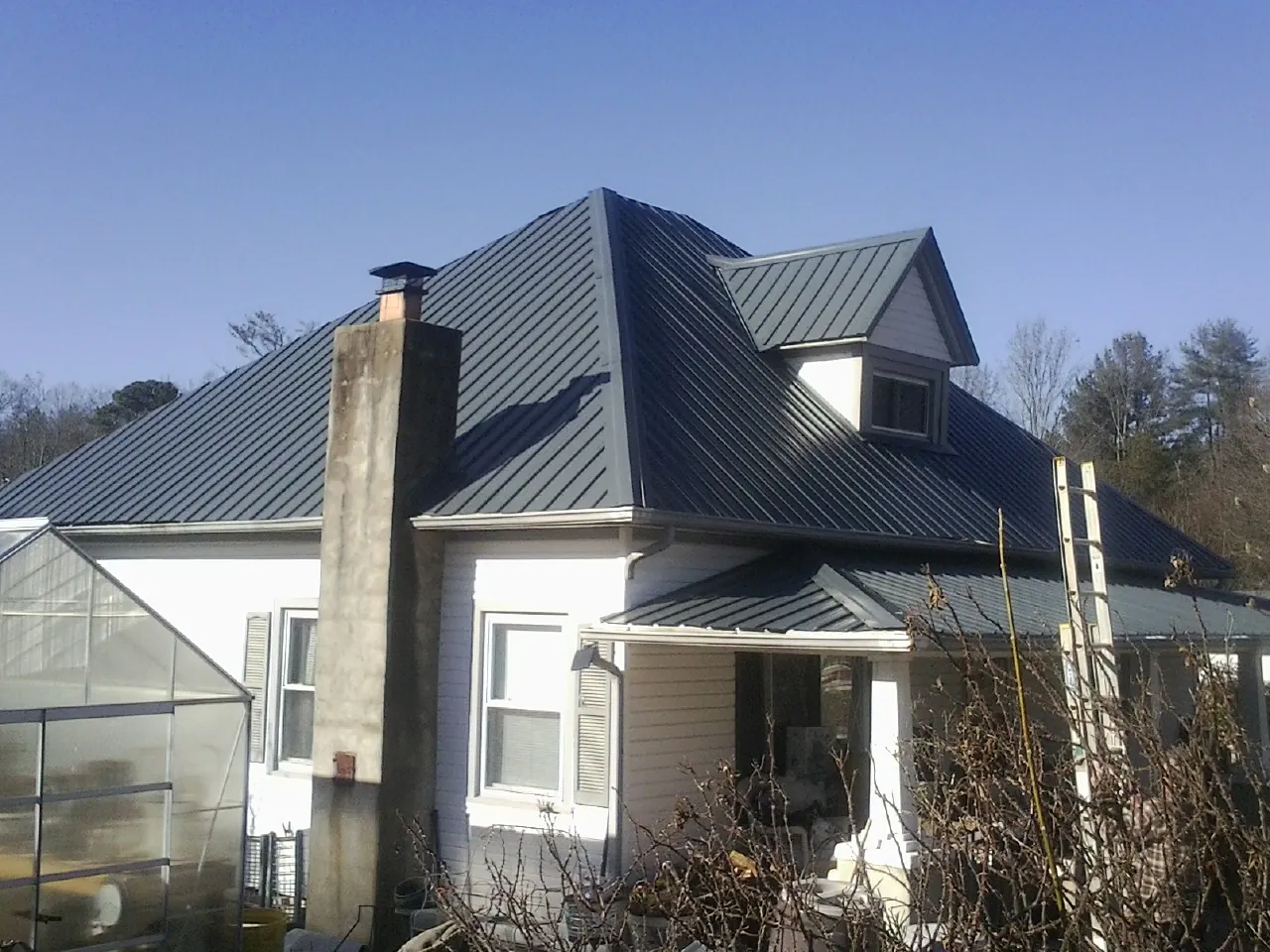Dark blue standing seam metal roof on a white farmhouse with dormer — Slate & Tile Roof Repair by Roofing Brothers in Retsof