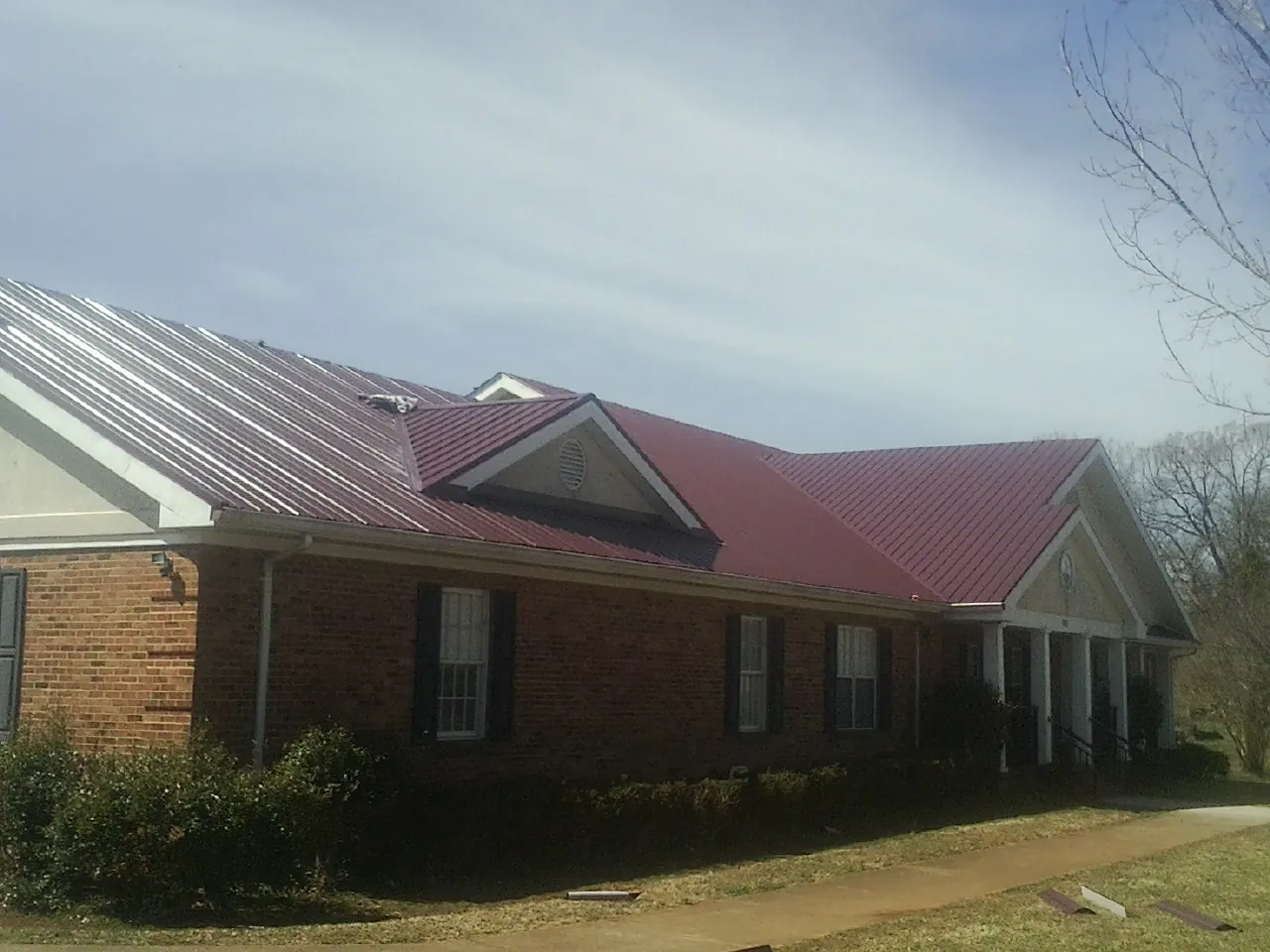 Red metal roof with gabled entries on a long brick building, from a Hail Damage Roof Repair job in Retsof